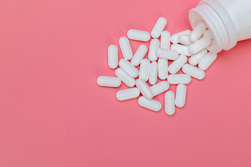 Medicine pills with white bottle on pink background.