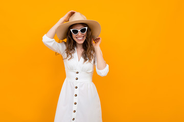 stylish girl in a straw hat with sunglasses dressed in a white dress on a yellow background with...
