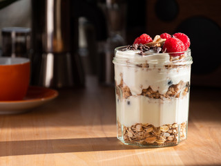 Fresh musli served with yoghurt, fresh raspberries, almonds and chocolate nibs in the jar on the table. Healthy breakfast.