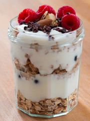 Fresh musli served with yoghurt, fresh raspberries, almonds and chocolate nibs in the jar on the table. Healthy breakfast.