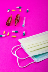 Protective face mask on pink background, pills, needle
