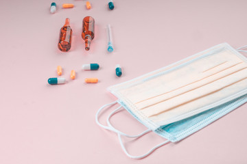 Protective face mask on pink background, pills, needle