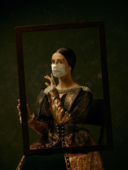 Medieval young woman as a duchess wearing protective mask against coronavirus spread on dark blue background. Concept of comparison of eras, healthcare, medicine and prevention against pandemic.