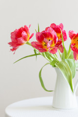 Red tulips bouquet in white vase on light background. Holiday background, close up. Valentine Day, Mothers day, birthday concept. Side view
