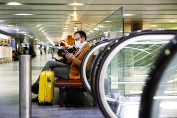 Man in mask at empty airport with luggage in coronavirus quarantine isolation, waiting for...