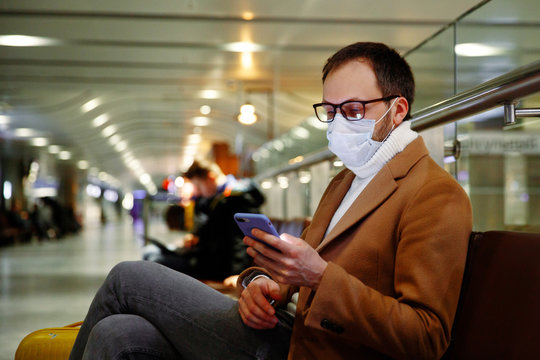 Man in mask at empty airport holding phone in coronavirus quarantine isolation, waiting for departure, flight cancellation, pandemic infection worldwide spread, travel restrictions and border shutdown