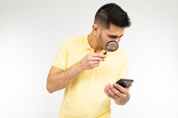 a man in a t-shirt holds a magnifying glass and a phone on a white background with copy space