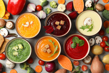 Vegetable soups and ingredients on grey background, top view