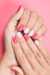 Closeup top view vertical photography of two beautiful female hands with trendy stylish bright colourful asymmetrical naildesign. White woman happy to show her fresh professional spa salon manicure.