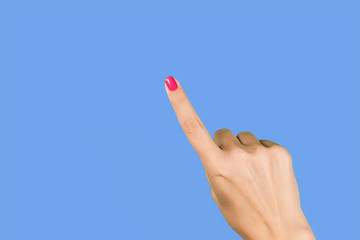 Closeup view photography of one manciured beautiful female hand making gesture by single index finger as if showing or pointing at something invisible isolated on blue background.