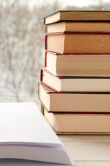 Old multi-colored books stand on a wooden shelf against the backdrop of the winter forest
