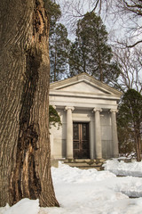 Mausoleum in a graveyard in winter next to a tree