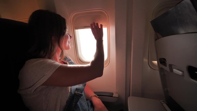 The girl opens the curtain of the illuminator on the plane in the evening.