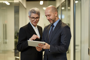 Waist up portrait of successful mature woman talking to colleague in modern office interior, copy space