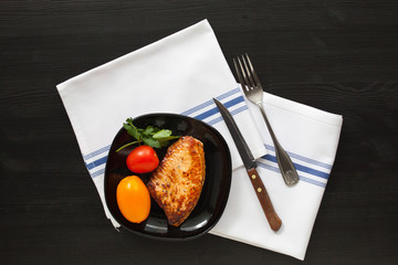 Fried  turkey steak on a black plate with tomatoes