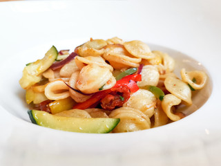Vegetarian pasta cooked with mixture of vegetables, like zucchini, red and green pepper, onion and dried tomatoes served in white plate