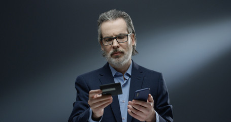 Gray haired man using smartphone and credit card.
