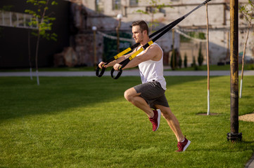 One man doing suspension straps exercises open air. Home workout routine.