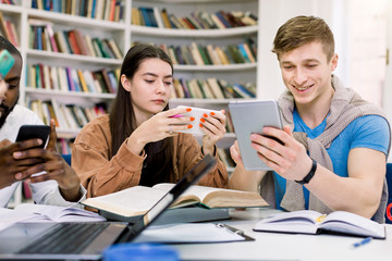 Multiethnic friends, college students are studying in library and using their gadgets, smartphone and tablet while having break during preparation for exams. Books, laptop and notepads on the table