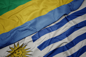 waving colorful flag of uruguay and national flag of gabon.