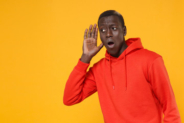 Curious young african american man guy in red streetwear hoodie posing isolated on yellow...