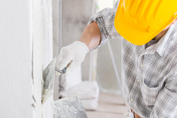 Builder using a trowel to add plaster to a wall - 332438821