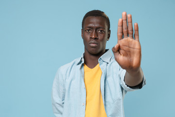 Fototapeta premium Concerned young african american man guy in casual shirt, yellow t-shirt posing isolated on blue background in studio. People lifestyle concept. Mock up copy space. Showing stop gesture with palm.