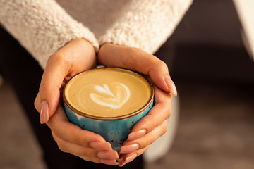 Beautiful female hands holding a blue cup with cappuccino.
