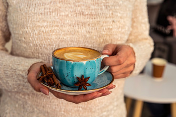 Beautiful female hands holding a blue cup with cappuccino.