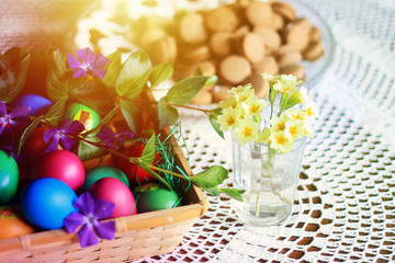 Easter colorful eggs, flowers, easter decor, red ceramic teapot and white tea-set with butterflies, home made cookies on a white knitted tablecloth in shabby chic kitchen, country style.