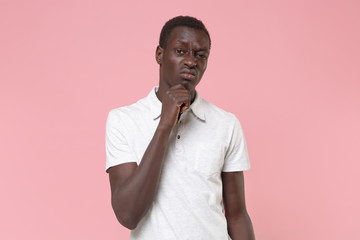 Confused young african american man guy in white polo shirt posing isolated on pastel pink...
