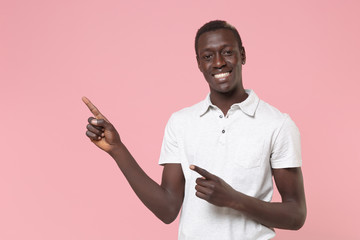 Smiling young african american man guy in white polo shirt posing isolated on pastel pink background studio portrait. People lifestyle concept. Mock up copy space. Pointing index fingers aside up.