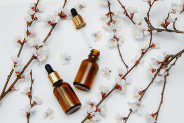 cosmetic bottles made of brown glass with a pipette on a white background with cherry blossoms on the branches with an empty space for text, copy space, flat lay, the concept of self-care, face, hands