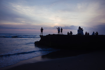 Fototapeta na wymiar Menschen auf felsen am Strand bei sonnenuntergang 