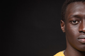Cropped image of young african american man guy in yellow t-shirt posing isolated on black background studio portrait. People sincere emotions lifestyle concept. Mock up copy space. Looking camera.
