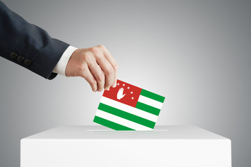 Man putting a voting ballot into a box with Abkhazia flag.