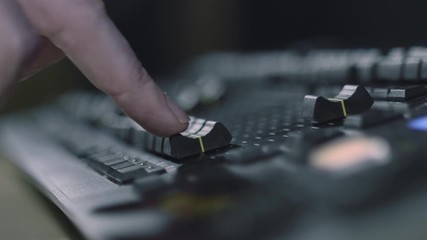 A lighting technician adjusting the sliders on a lighting desk panel - close up