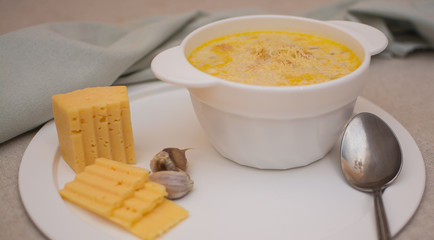 Puree soup with cheese in a white ceramic bowl on a white metal tray.