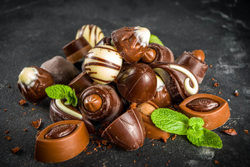 Various chocolate candies over dark background. Different sweet and chocolates with mint leaves,...