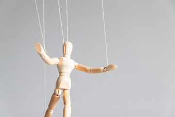 Human control concept. Wooden puppet doll on the clothesline on a gray background with copy space.