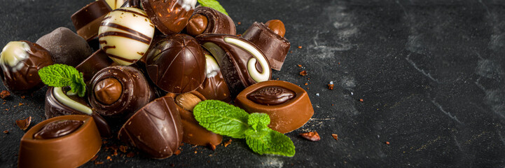 Various chocolate candies over dark background. Different sweet and chocolates with mint leaves, copy space