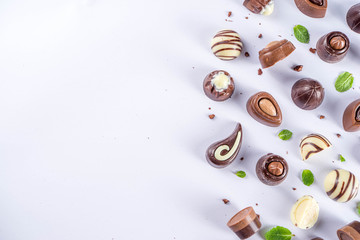 Various chocolate candies over white background. Different sweet and chocolates with mint leaves, copy space, simple pattern layout