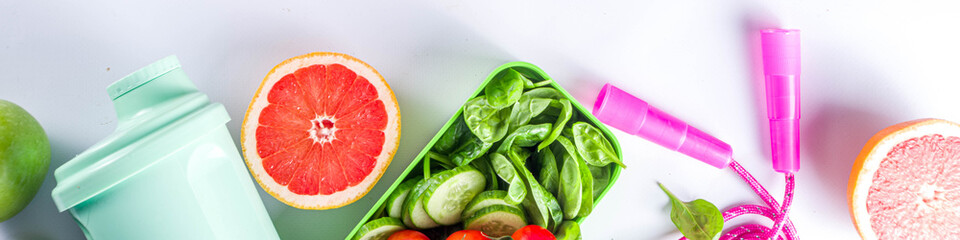 Fitness and healthy food lifestyle concept. Dumbbells, diet fruit and vegetable lunch box, water and jump rope on white background. Flatlay image, top view copy space