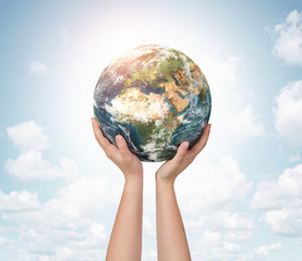 Child hands holding planet earth over blue sky background with copy space