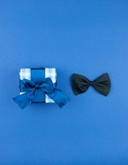 Happy Fathers day concept. Gift box with bow tie over dark blue paper background. Top view. International men's day concept.