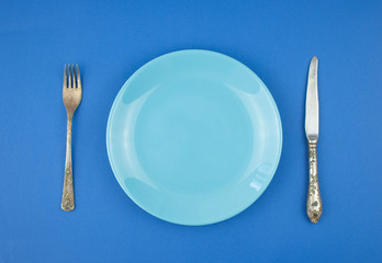 Empty plate with a cutlery on the blue paper background