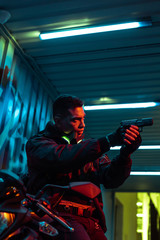 Fototapeta na wymiar mixed race cyberpunk player aiming gun near motorcycle