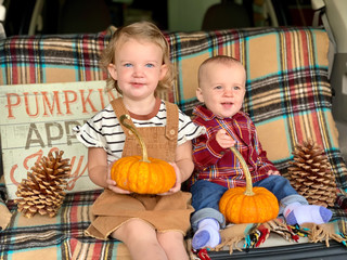 Fototapeta premium Brother and sister holding pumpkins in back of family car