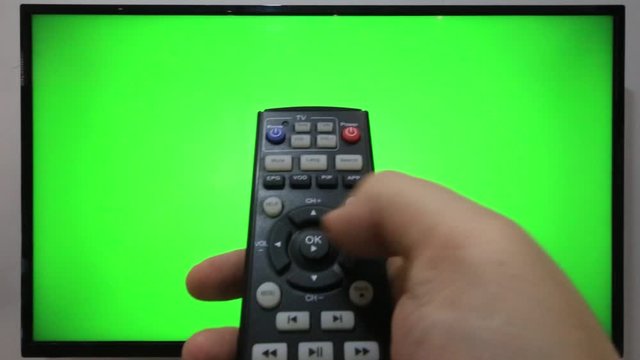 Person pointing a TV remote and pressing buttons in front of a TV with green screen