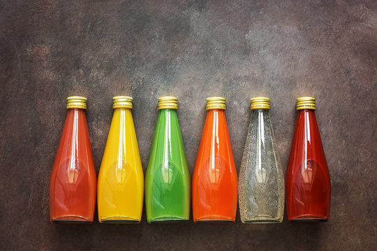 Assorted various colored drinks in bottles on a dark rustic background, border. Top view, flat lay.